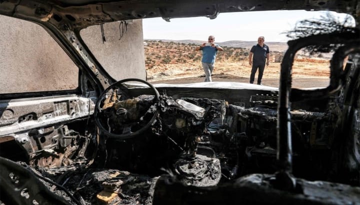 Men stand near a vehicle that was reportedly torched by Israeli settlers during an overnight attack on the Palestinian Christian village of Taybeh. Photo: Zain JAAFAR