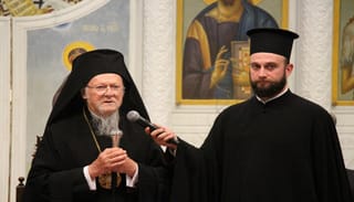 Patriarch Bartholomew speaks to members of YAL as Patriarchal Deacon Barnabas Grigoriadis holds the microphone.