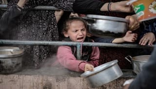 Palestinian children in Rafah wait in line on Feb. 10 among the rubble of destroyed buildings to receive food prepared for Palestinian families displaced to southern Gaza due to Israeli