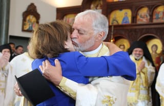Fr. Alex Karloutsos kisses his wife, Xanthi, after being elevated to the rank of Megas Protopresbyteros. Photo: Aaron Hickman/UOJ