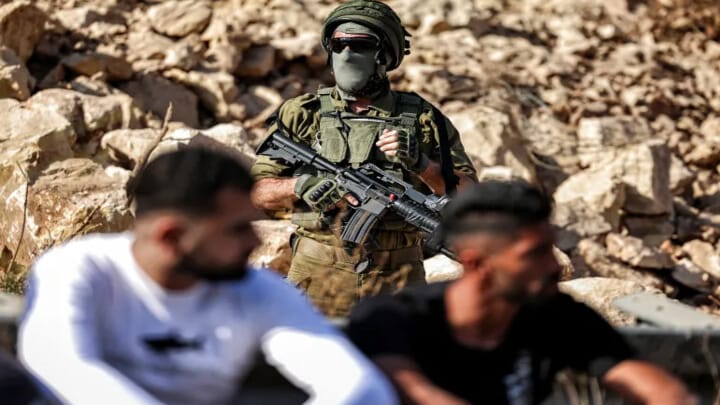 An Israeli soldier stands guard as Palestinians gather in protest at the site of a new road under construction for the use of Israeli settlers near the Palestinian village of Beit Ur